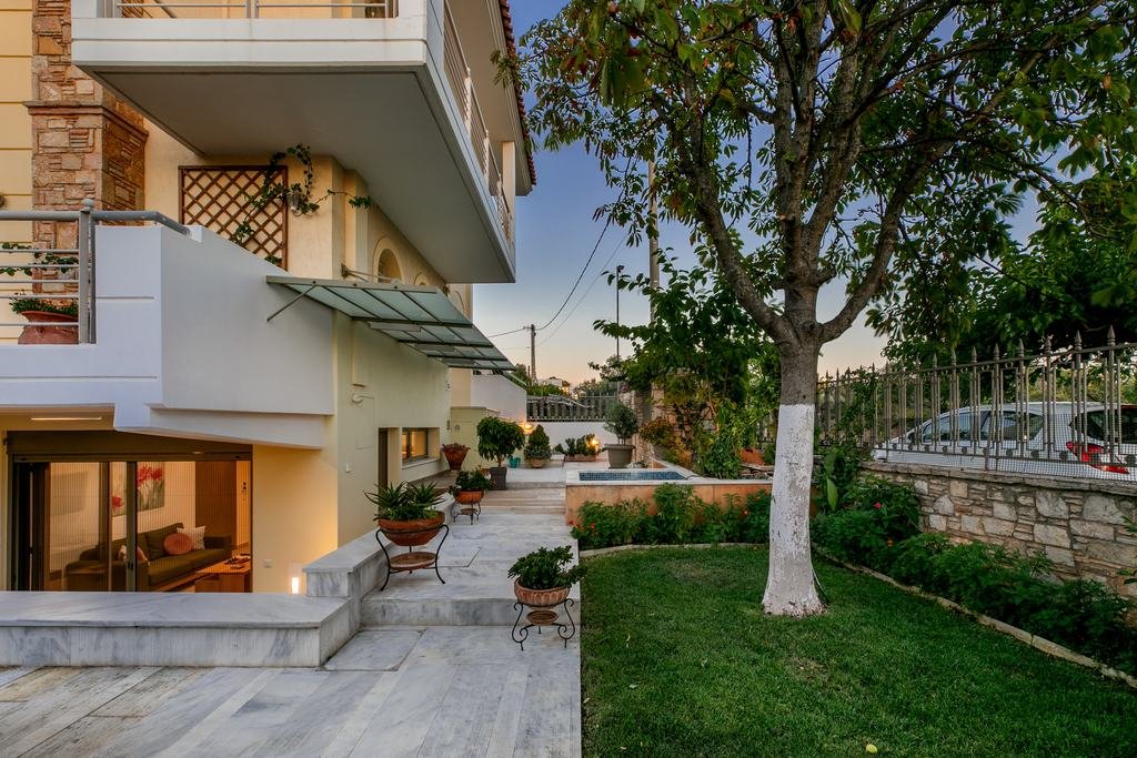 The house at dusk, with the lit garden-level apartment, marble courtyard, lawn and a white-trunked tree