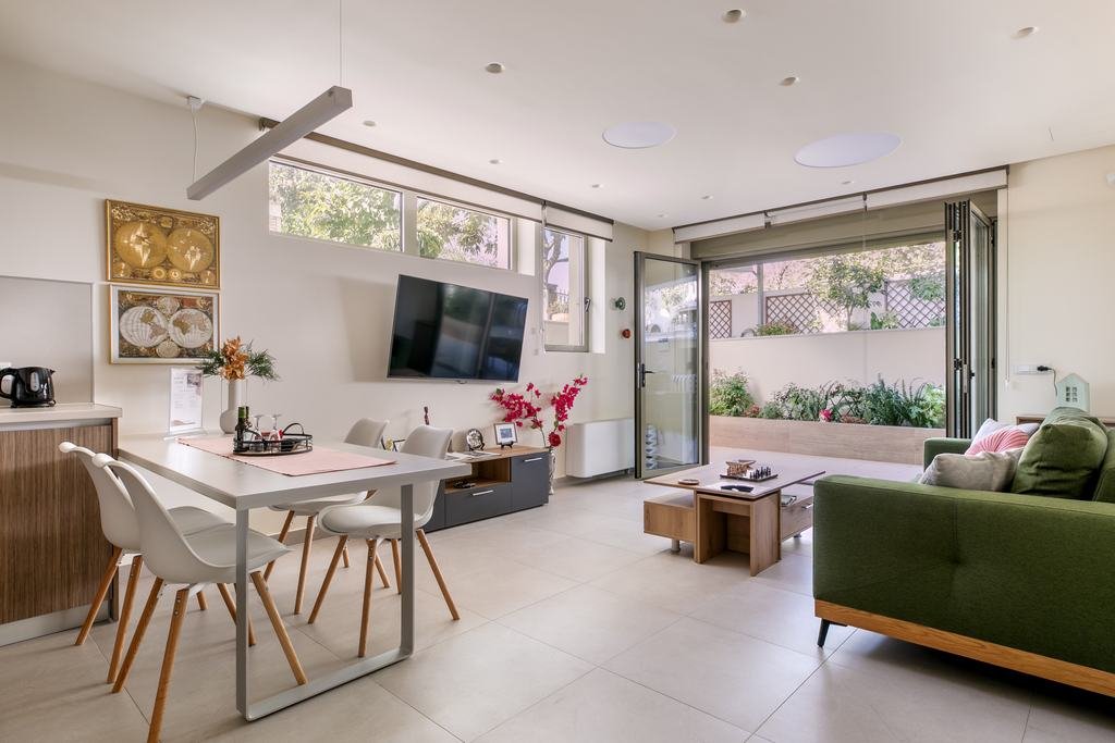 Bright open-plan living room with a dining table, a green sofa and glass doors folded open to the patio