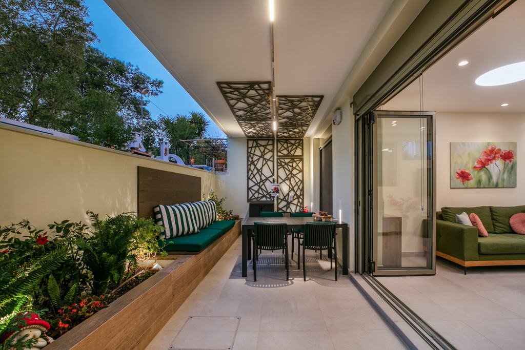 Covered patio at dusk with laser-cut pergola panels, a dining table and green benches, open to the living room
